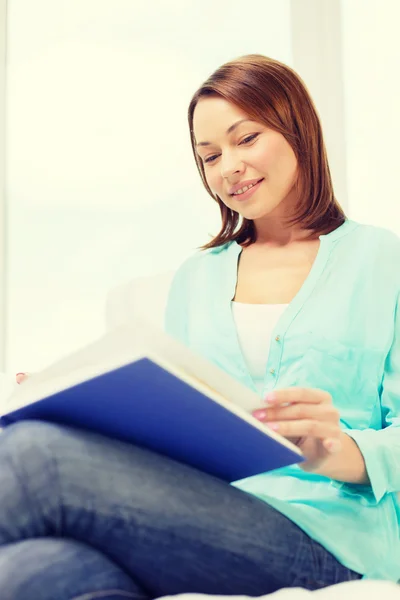 Mujer sonriente leyendo libro y sentada en el sofá — Foto de Stock