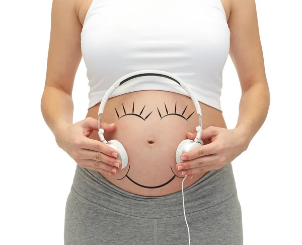 Gros plan de la femme enceinte et écouteurs sur le ventre — Photo