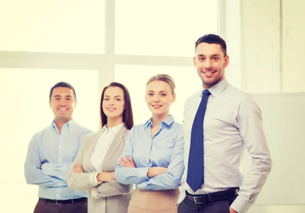 Empresário sorridente no cargo com equipe nas costas — Fotografia de Stock