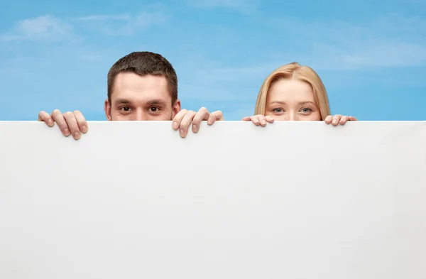 Happy couple hiding behind big white blank board — Stock Photo, Image