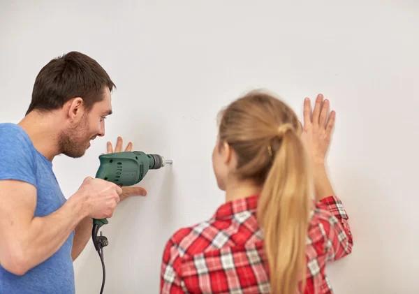 Feliz pareja con taladro perforando pared en casa —  Fotos de Stock