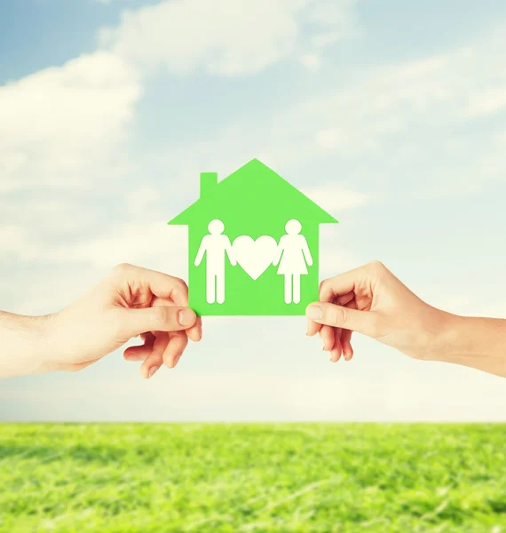 Руки держат зеленый дом с семьей — стоковое фото