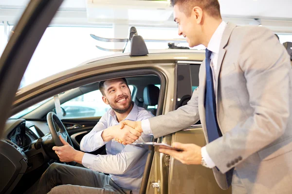 Šťastný muž s prodejci aut v autosalonu nebo salónek — Stock fotografie