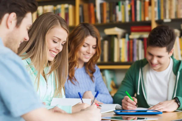 Šťastní studenti zápis do notebooků v knihovně — Stock fotografie