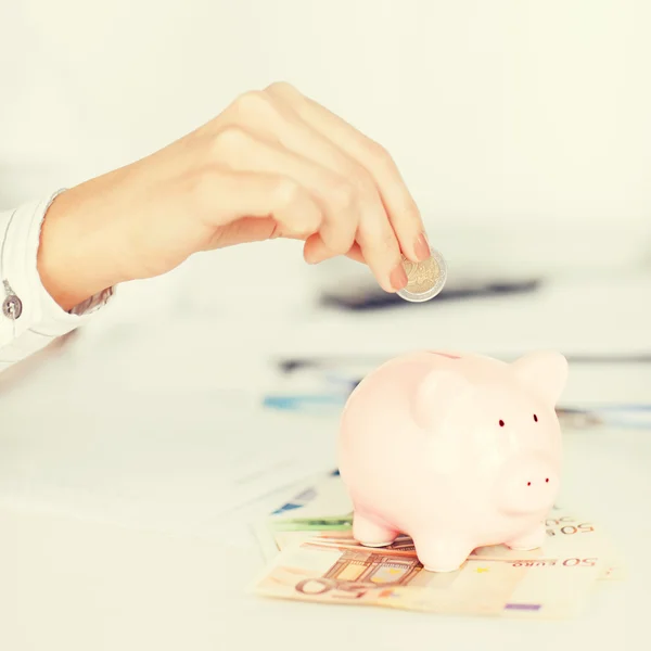Woman hand putting coin into small piggy bank — Stock Photo, Image