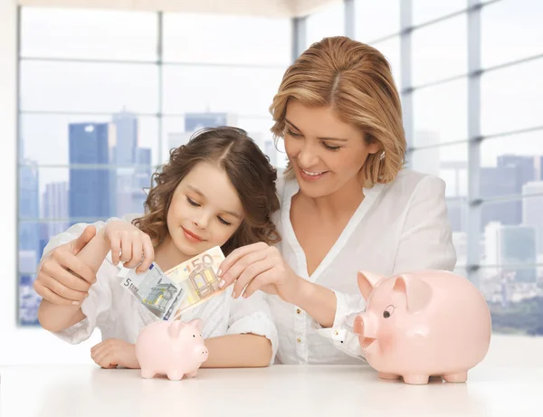 Мать и дочь вкладывают деньги в копилки — стоковое фото