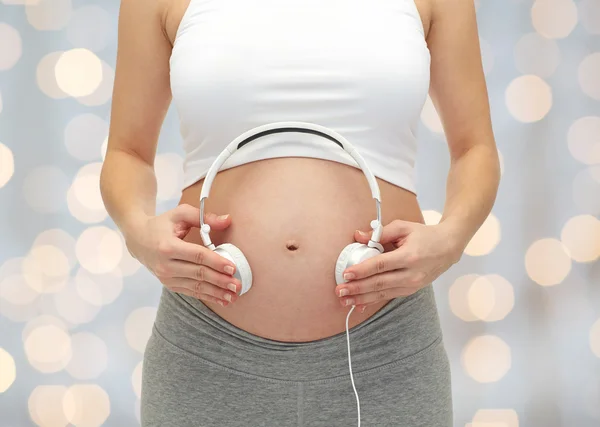 Primo piano della donna incinta e cuffie sulla pancia — Foto Stock