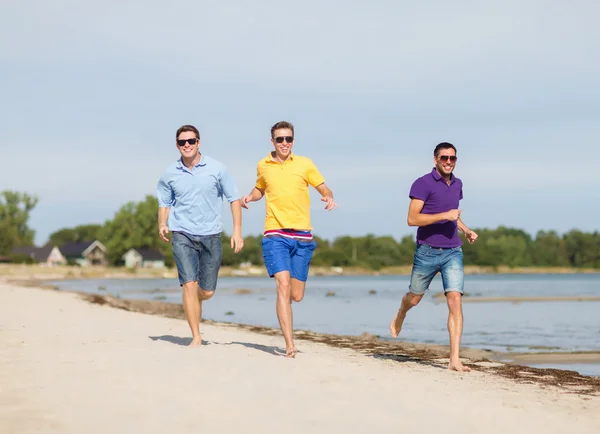 Amigos sonrientes en gafas de sol corriendo por la playa —  Fotos de Stock