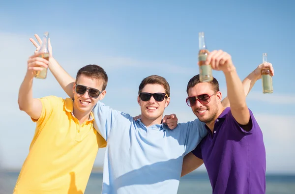 Glada vänner med ölflaskor på stranden — Stockfoto