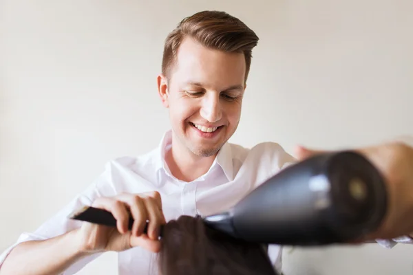 Estilista feliz com ventilador fazendo blow-dry no salão — Fotografia de Stock