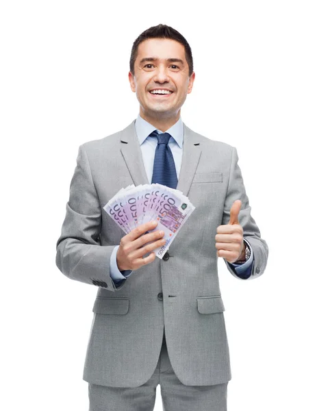 Smiling businessman with money showing thumbs up — Stock Photo, Image