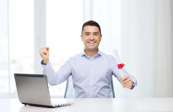 Uomo sorridente con diploma e computer portatile in ufficio — Foto Stock