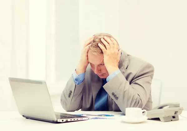 Upset older businessman with laptop and telephone — Stock Photo, Image