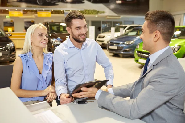 Couple heureux avec concessionnaire de voitures en salon ou salon de l'auto — Photo