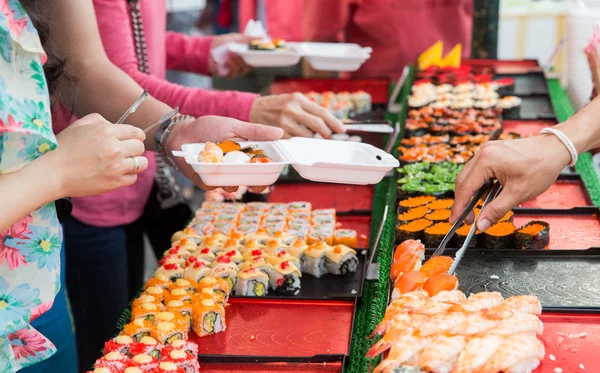 Close up of hands with tongs taking sushi — Stock Photo, Image