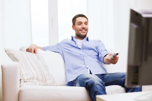 Uomo sorridente con telecomando tv a casa — Foto Stock