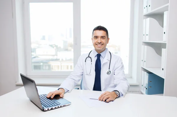 Улыбающийся врач-мужчина с ноутбуком в медицинском кабинете — стоковое фото