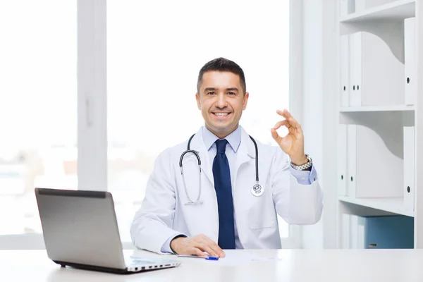 Sonriente médico con el ordenador portátil mostrando ok en la oficina —  Fotos de Stock