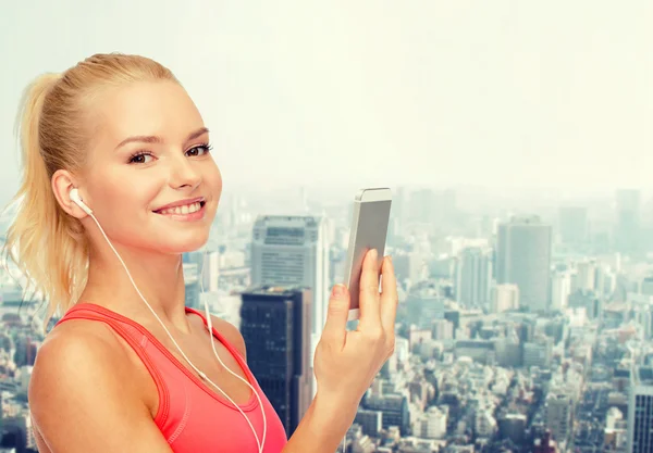 Sorrindo mulher desportiva com smartphone e fones de ouvido — Fotografia de Stock