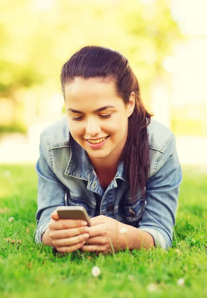 Glimlachend jong meisje met smartphone liggen op gras — Stockfoto