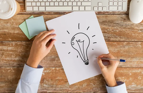 Close up of hands drawing lighting bulb on paper — Stock Photo, Image