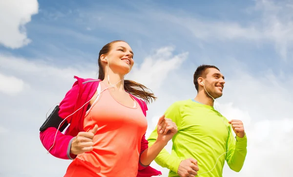 Sonriente pareja con auriculares corriendo al aire libre — Foto de Stock