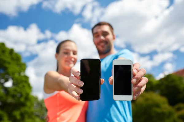 Dos personas sonrientes con teléfonos inteligentes al aire libre — Foto de Stock