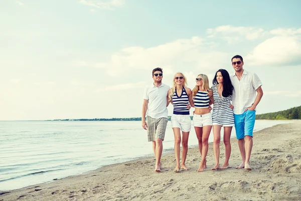 Lachende vrienden in zonnebril wandelen op het strand — Stockfoto