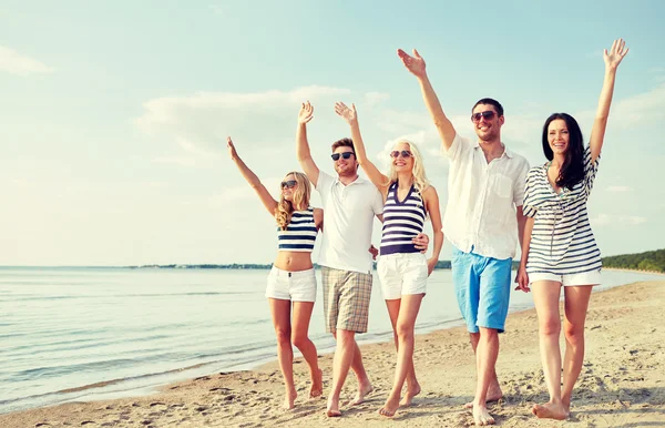 Amici sorridenti che camminano sulla spiaggia e salutano le mani — Foto Stock