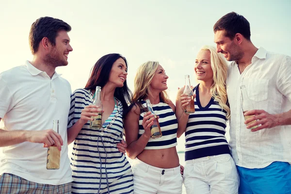 Smiling friends with drinks in bottles on beach — Stock Photo, Image