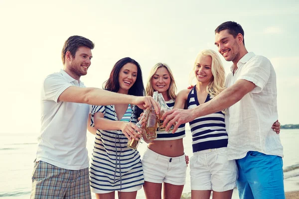 Smiling friends clinking bottles on beach — Stock Photo, Image