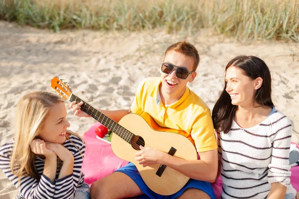 Groep gelukkige vrienden spelen gitaar op strand — Stockfoto