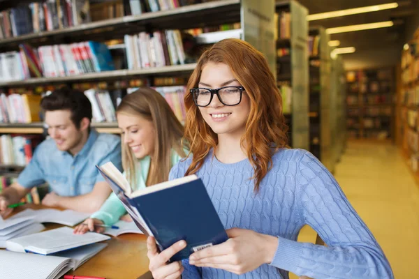 Estudantes felizes lendo livros na biblioteca — Fotografia de Stock