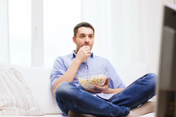 Ung man titta på tv och äta popcorn hemma — Stockfoto