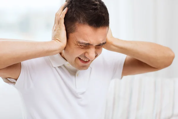 Hombre infeliz cerrando sus oídos por las manos en casa —  Fotos de Stock