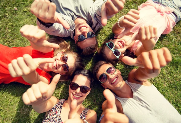 Lachende vrienden tonen duimschroef opwaarts liggen op gras — Stockfoto