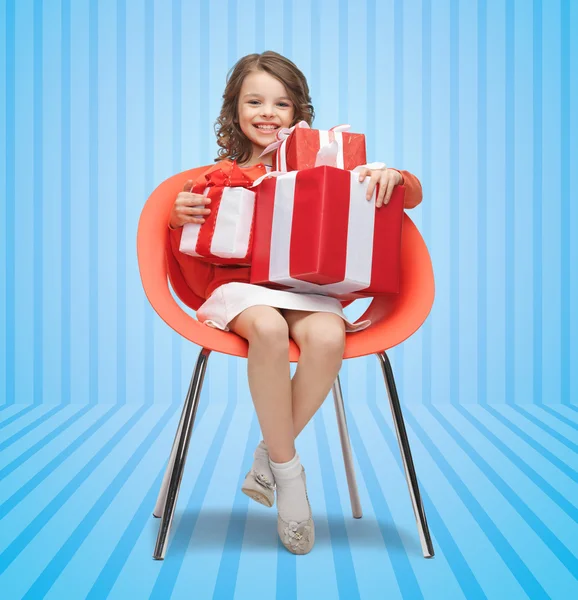 Happy little girl with gift boxes sitting on chair — Stock Photo, Image