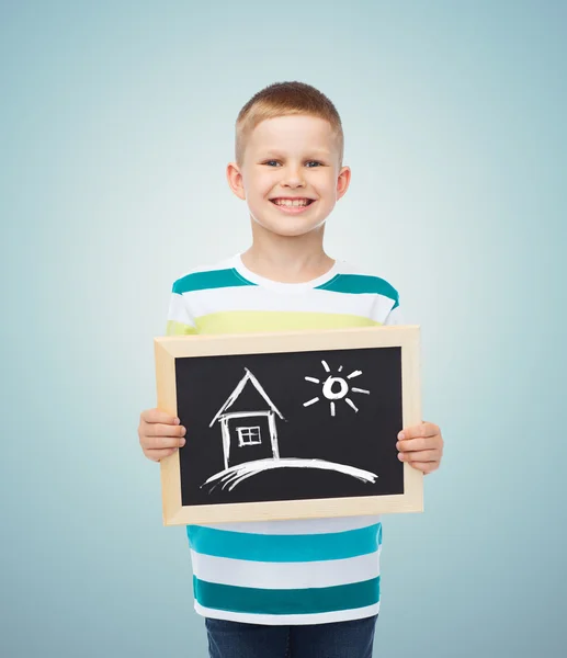 Happy little boy holding chalkboard with home — Stock Photo, Image