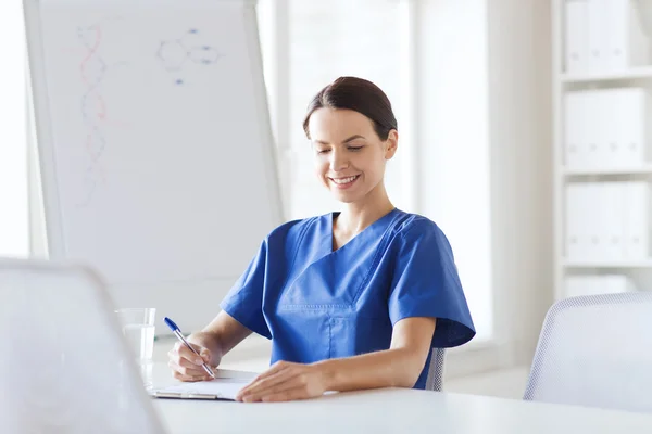 Happy female doctor or nurse writing to clipboard — Stock Photo, Image