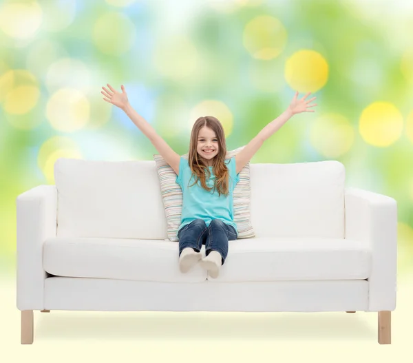 Happy girl sitting on sofa with raised hands — Stock Photo, Image