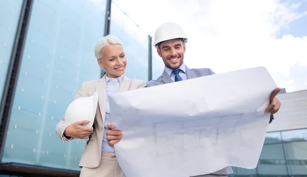 Smiling businessmen with blueprint and helmets — Stock Photo, Image