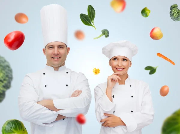 Feliz pareja de cocineros o cocineros sobre fondo de alimentos —  Fotos de Stock