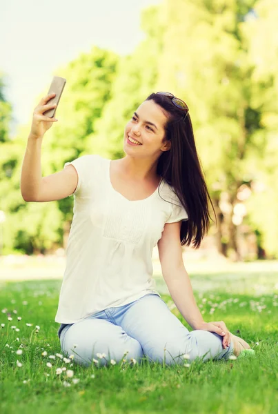 S úsměvem mladá dívka s smartphone sedí v parku — Stock fotografie