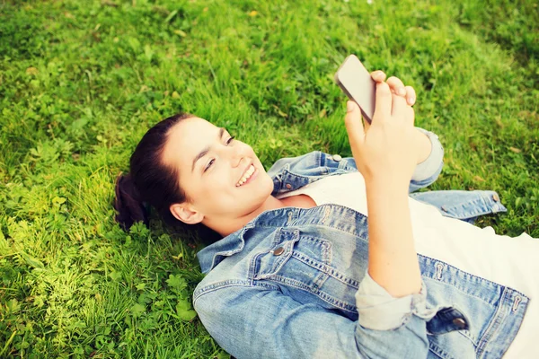 Glimlachend jong meisje met smartphone liggen op gras — Stockfoto