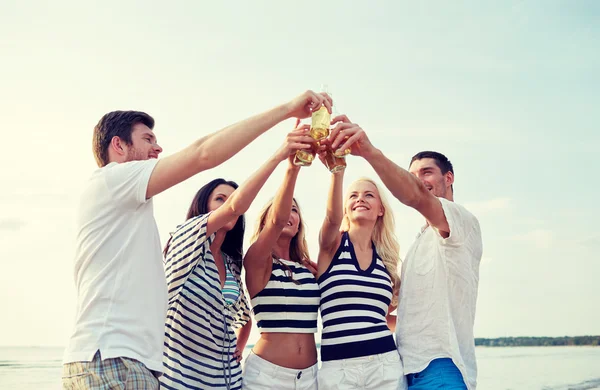 Amis souriants bouteilles cliquetis sur la plage — Photo