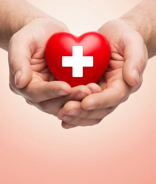Mãos masculinas segurando coração vermelho com cruz branca — Fotografia de Stock