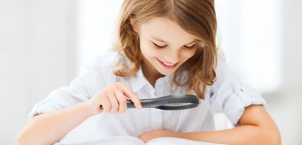 Girl reading book with magnifier at school — Stock Photo, Image