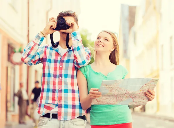 Coppia sorridente con mappa e macchina fotografica in città — Foto Stock