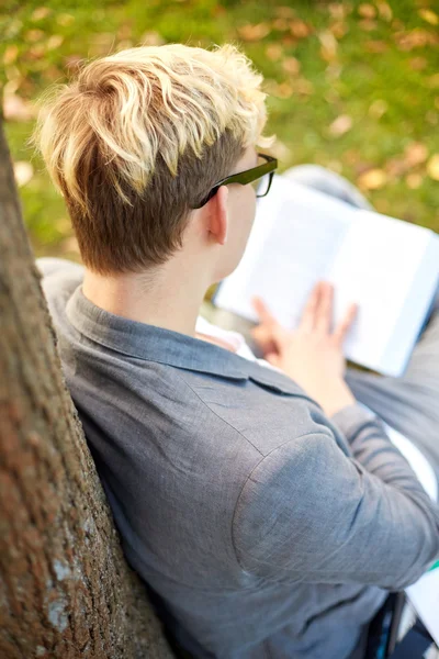 Teenage boy or young man reading book outdoors — Stock Photo, Image