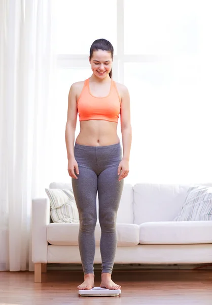 Happy young woman weighing on scales at home — Stock Photo, Image